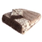 Dwustronny koc bawełniany 150x200 cm w odcieniach beżowo-brązowych z frędzlami, złożony na boku. Wzór mozaikowy jest widoczny, a miękka faktura materiału sugeruje komfort i ciepło. Koc idealny do aranżacji w salonie lub sypialni.