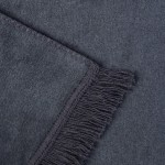 Koc bawełniany 150x200 cm w ciemnoszarym kolorze, z frędzlami na jednym z brzegów. Zdjęcie w zbliżeniu, ukazujące teksturę materiału oraz detale wykończenia. Koc leży na powierzchni o miękkiej fakturze, co podkreśla jego właściwości.