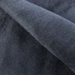 Koc bawełniany 150x200 z frędzlami w ciemnoszarym kolorze, leżący w złożeniu, prezentuje gładką, teksturowaną powierzchnię. Frędzle na brzegach dodają dekoracyjnego akcentu. Tło jest jednolite, co podkreśla detal produktu.