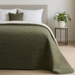 Zielona narzuta Verde mink 170x210 z pikowanym wzorem, leżąca na łóżku. Widoczna dekoracyjna poduszka w tym samym odcieniu. W tle jasna ścianka i stół z rośliną. Narzuta ma delikatną fakturę. Ułożona bez fałd, w pełni rozłożona.