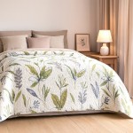 Narzuta Flori 170x210 w kolorach białym z zielonymi i szaro-niebieskimi roślinnymi wzorami, leży na łóżku. W tle widoczne poduszki oraz lampka nocna. Narzuta ma pikowaną teksturę. Wnętrze jest jasne i przytulne.