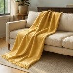 Koc bawełniany 150x200 w intensywnym żółtym kolorze, o teksturowanej powierzchni, z frędzlami na dolnej krawędzi. Produkt leży na jasnoszarym, tapicerowanym sofie w jasnym wnętrzu, w otoczeniu roślinności. Widoczny kąt ujęcia frontalny.