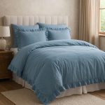 Pościel bawełniana z falbanką 160x200 w kolorze błękitnym, rozłożona na łóżku z jasnym materacem. Widoczne dwie poduszki również w błękitnym odcieniu z falbankami. Tło jasne, neutralne, podkreślające kolorystykę pościeli.
