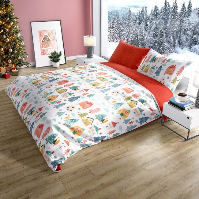 Pościel bawełniana 220x200 z kolorowym wzorem świątecznych domków i choinek na białym tle. Poduszki w intensywnej czerwieni. Ułożona na łóżku w jasnym wnętrzu, z widokiem na zimowy krajobraz przez okno.