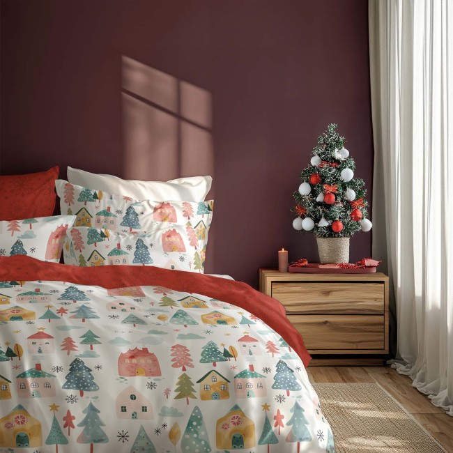 Pościel bawełniana świąteczna 220x200 z kolorowymi domkami i choinkami na białym tle, w odcieniach czerwieni i zieleni. Złożona na łóżku, obok mała choinka w doniczce i świeca na stoliku nocnym. Tło w kolorze burgundowym.