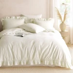 Pościel bawełniana w kolorze białym, rozmiar 220x200 cm, z falbanką na krawędzi. W zestawie cztery poduszki w różnych rozmiarach. Ułożona na łóżku w jasnym wnętrzu, z książką na pościeli i dekoracyjnym wazonem obok.