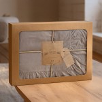 Pościel bawełniana w odcieniu zieleni butelkowej z falbanką, w rozmiarze 160x200 cm. Pakowana w eleganckie pudełko z brązowym wykończeniem, z widoczną etykietą i dekoracyjnym sznurkiem. Tło jasne, drewniany stół.