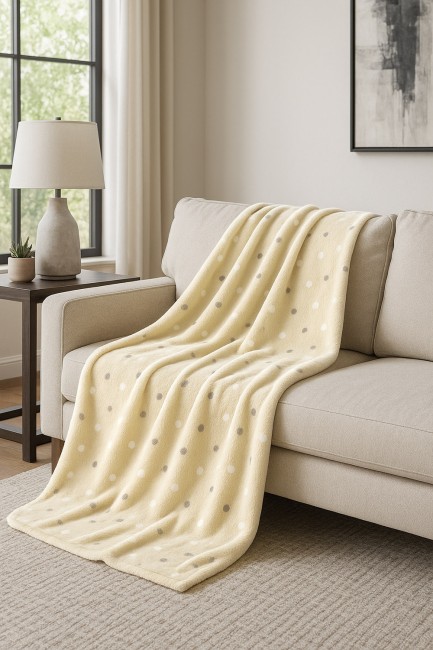 Puszysty koc dekoracyjny w kolorze żółtym z wzorem w kropki, o wymiarach 200x220 cm, leżący na beżowej kanapie. Koc ma miękką fakturę, idealny do wnętrz, tworząc przytulną atmosferę. W tle widoczna lampa i roślina.