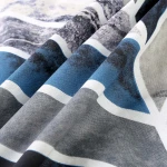 Pościel bawełniana 220x200 cm w odcieniach niebieskiego, z geometrycznym wzorem w białe i ciemnoszare akcenty. Tkanina o gładkiej fakturze, ukazana w zbliżeniu, z widocznymi fałdami, co podkreśla jej miękkość i jakość.