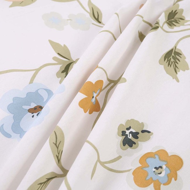 Pościel bawełniana 140x200 Meadowe w białym kolorze z kolorowym kwiatowym wzorem. Zbliżenie na tkaninę ukazującą detale niebieskich, pomarańczowych i zielonych kwiatów oraz liści, o gładkiej fakturze.