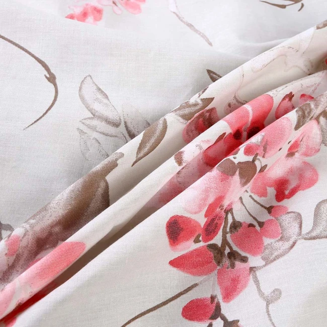 Pościel bawełniana 180x200 cm w odcieniach beżu z różowymi kwiatami. Materiał gładki, lekko transparentny, ukazujący delikatne detale florystyczne. Ułożona w sposób luźny, z widocznymi wzorami i liśćmi w odcieniach brązu.