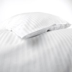 Pościel hotelowa bawełniana 220x200 cm w białe pasy 1 cm, ułożona na łóżku z poduszką. Materiał gładki, z delikatnym połyskiem. Widoczna poduszka w tym samym wzorze, leżąca na poszwie. Tło białe, co podkreśla elegancję tekstyliów.