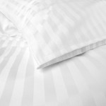 Pościel hotelowa bawełniana 220x200 w białe pasy 2 cm, z poduszką, lekko złożona na białym tle. Materiał gładki, z delikatnym połyskiem. Widoczny kontrast tekstury zebrań na tkaninie. Poduszka elegancko wykończona, prezentuje zakładkę 30 cm.