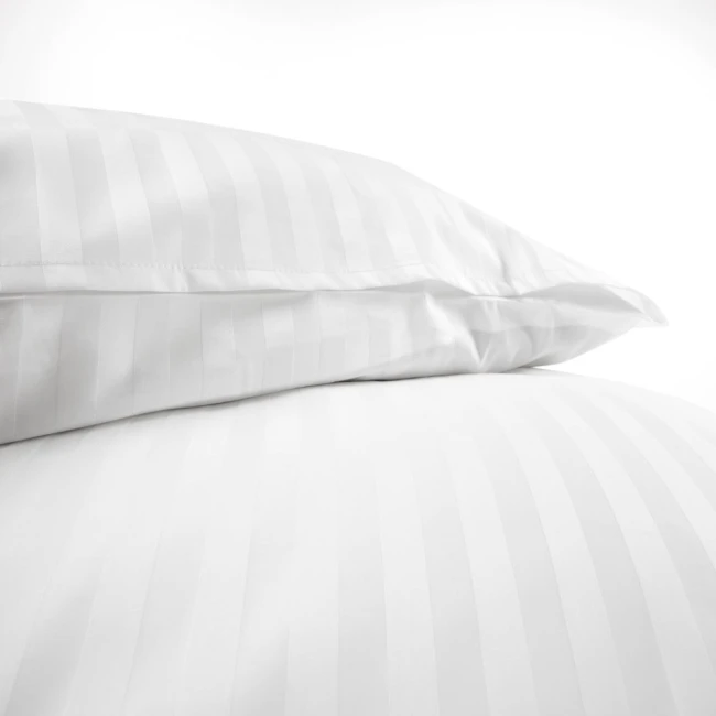 Pościel hotelowa bawełniana 220x200 w białe pasy 2-cm, z zakładką 30 cm. Widok z dołu na poszwę i poduszki, ułożone blisko siebie na gładkim tle. Materiał gładki, z delikatnym wzorem pasków, idealny do eleganckiej aranżacji sypialni.