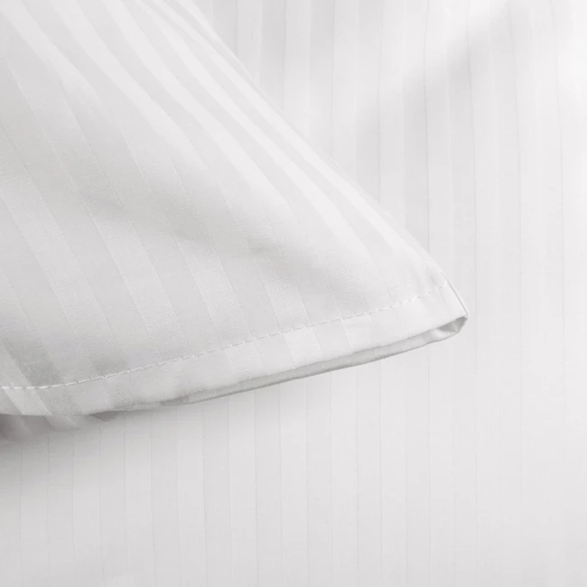 Poszewka na poduszkę 70x80 cm w kolorze białym z delikatnym, 1-centymetrowym wzorem w paski. Ujęcie z boku, ukazujące narożnik poszewki. Materiał gładki, z wykończeniem na zakładkę, bez widocznych napisów czy logo. Tło proste, białe.