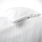 Poszewka hotelowa na poduszkę 70x80 cm, biała w paseczki o szerokości 1 cm, leżąca w układzie złożonym. Materiał gładki, z delikatnym połyskiem, na jednolitym tle. Widoczne szwy i krawędzie, brak napisów oraz logo.