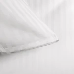 Biała poszewka na poduszkę 50x70 cm w paski 1 cm, z zakładką. Zbliżenie na krawędź, ukazujące teksturę i detale. Gładki materiał, prosty wzór. Produkt leży na jednolitym tle.