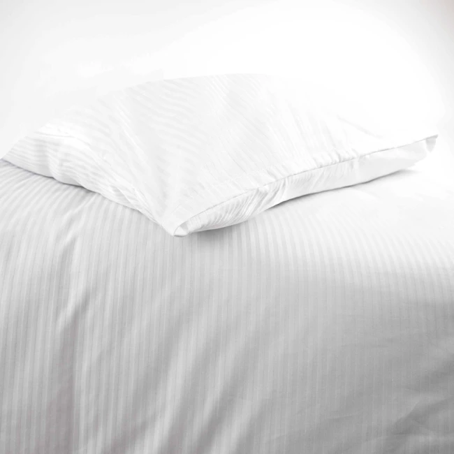 Poszewka na poduszkę 70x80 cm hotelowa, w białym kolorze z delikatnym paskiem 4 mm, leży na podłożu. Produkt jest złożony, a jego faktura jest gładka. Tło jest jasne i jednolite, co podkreśla prostotę designu.