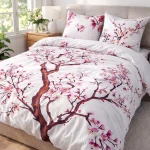 Pościel satynowa w rozmiarze 180x200 cm z białym tłem ozdobionym wzorem drzewa wiśniowego i różowymi kwiatami. Poduszki z tym samym motywem. Ułożona na łóżku, w otoczeniu lampy nocnej i kosza.