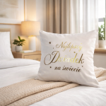 Poszewka dekoracyjna 40x40 cm w kolorze białym z napisem Najlepszy Dziadek na świecie w złotym kolorze, umieszczona na łóżku z beżowym pledem. Tło jasne, z roślinnością i lampką nocną w aranżacji wnętrza.