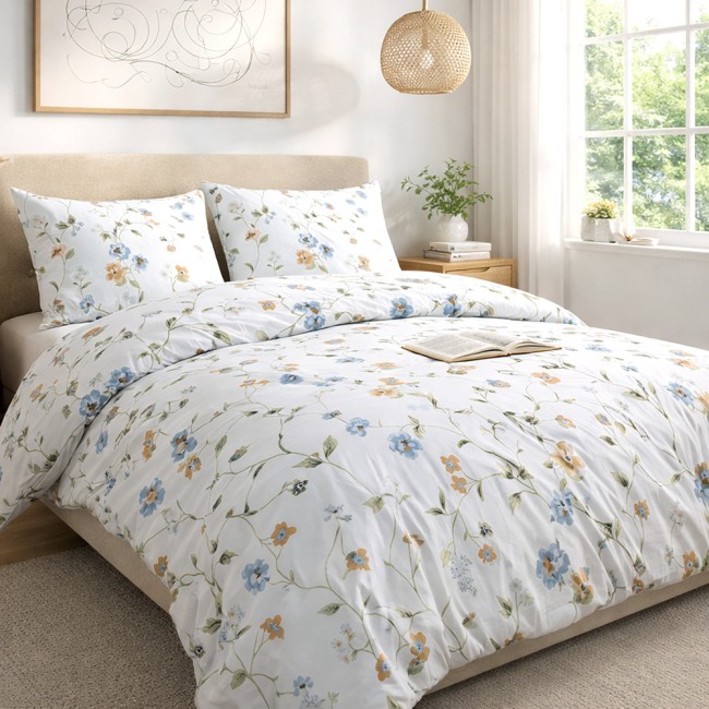 Pościel bawełniana 140x200 Meadowe w białym kolorze z kolorowymi kwiatami, złożona na łóżku. W zestawie dwie poduszki w tym samym wzorze. Tło jasne, z widocznym oknem i roślinnością, sprawiające wrażenie świeżości.