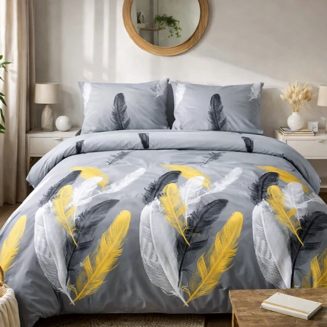 Pościel satyna bawełniana 140x200 w odcieniach białym, czarnym i złotym, z motywem piór na szarym tle. Widoczna zestaw składający się z narzuty i dwóch poszewek na poduszki, leżący na łóżku. Struktura materiału gładka, z wyrazistym wzorem.
