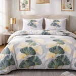 Pościel flanelowa 180x200 cm w kolorze szarym z wzorem liści miłorzębu. Pozycja rozwinięta na łóżku, widok frontalny. Narzuta i poduszki z delikatnym, teksturowanym tłem. Elementy dekoracyjne w kolorze żółtym i zielonym.