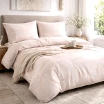 Pościel flanelowa w rozmiarze 160x200 cm w kolorze pudrowego różu z białym wzorem liści. Złożona narzuta na łóżku z poduszkami w tym samym stylu, prezentująca delikatny, kwiatowy motyw. Tło neutralne, w stylowym wnętrzu.