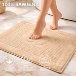 Dywanik łazienkowy 50x70 cm w kolorze cappuccino, wykonany z 100% bawełny, z teksturą frotte. Na powierzchni widoczny wzór stóp, idealny do szybkiej absorpcji wody. Ułożony na jasnej podłodze, z nagim stopą na dywaniku.