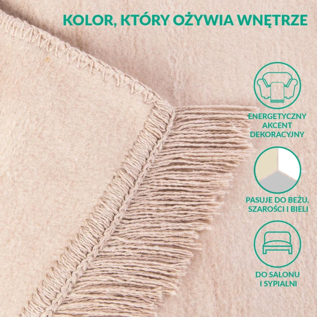 Koc bawełniany 200x220 w jasnym beżu, z frędzlami na jednym boku. Ujęcie w zbliżeniu, pokazujące fakturę materiału oraz detal wykończenia. Produkt leży na gładkiej powierzchni, z prostym tłem.