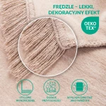 Koc bawełniany w jasnym beżu o wymiarach 200x220 cm, z frędzlami przy krawędzi. Ułożony w roli luźno rozłożonej, zbliżenie na delikatną fakturę materiału oraz detal ozdobny frędzli. Tło neutralne, podkreślające kolor i strukturę produktu.