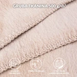 Jasny beżowy koc bawełniany 200x220 cm z frędzlami, złożony w górnej części widoku; faktura dzianiny widoczna z bliska, wyraźne szycie. Brak dodatkowych elementów na tle.