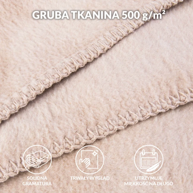 Jasny beżowy koc bawełniany 200x220 cm z frędzlami, złożony w górnej części widoku; faktura dzianiny widoczna z bliska, wyraźne szycie. Brak dodatkowych elementów na tle.