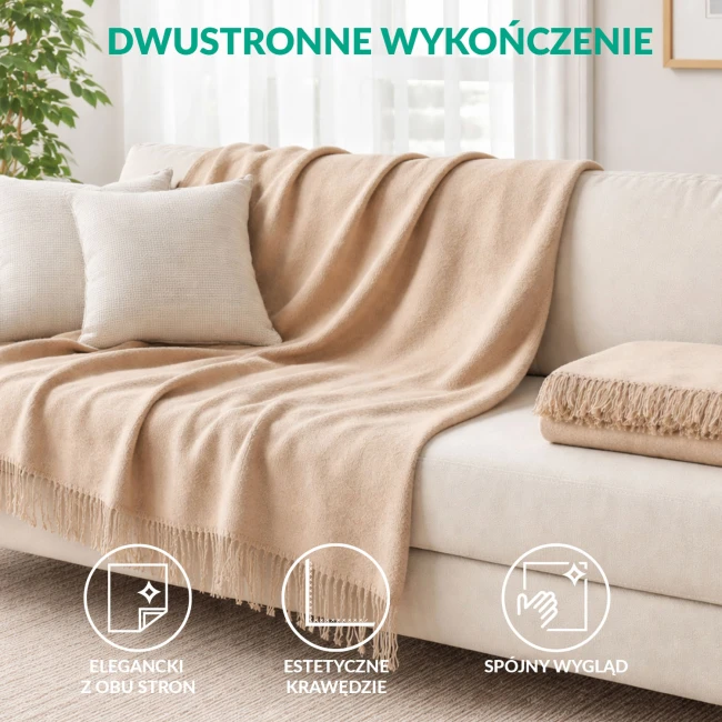 Koc bawełniany 200x220 w jasnym beżu, rozłożony na oparciu jasnoszarego fotela, z delikatnymi frędzlami na dolnej krawędzi. W tle widoczne okno oraz stół z rośliną w szklanym wazonie. Tło jasne i stonowane, podkreślające kolor koca.