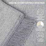 Koc bawełniany 150x200 cm w odcieniu szarym, z wyraźnymi frędzlami na jednym z brzegów. Materiał o lekko teksturowanej powierzchni, prezentowany w zbliżeniu na detal splotu i wykończenia, leży na jednolitym tle.