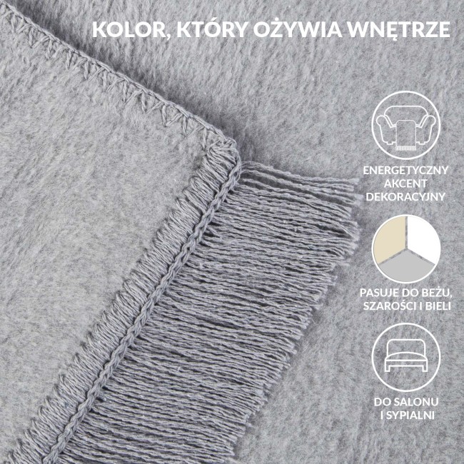 Koc bawełniany 150x200 cm w odcieniu szarym, z wyraźnymi frędzlami na jednym z brzegów. Materiał o lekko teksturowanej powierzchni, prezentowany w zbliżeniu na detal splotu i wykończenia, leży na jednolitym tle.