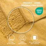 Koc bawełniany w kolorze żółtym 150x200 cm, z frędzlami, rozłożony na gładkiej powierzchni, z widoczną, teksturowaną tkaniną i starannym wykończeniem krawędzi. Frędzle dodają charakteru.