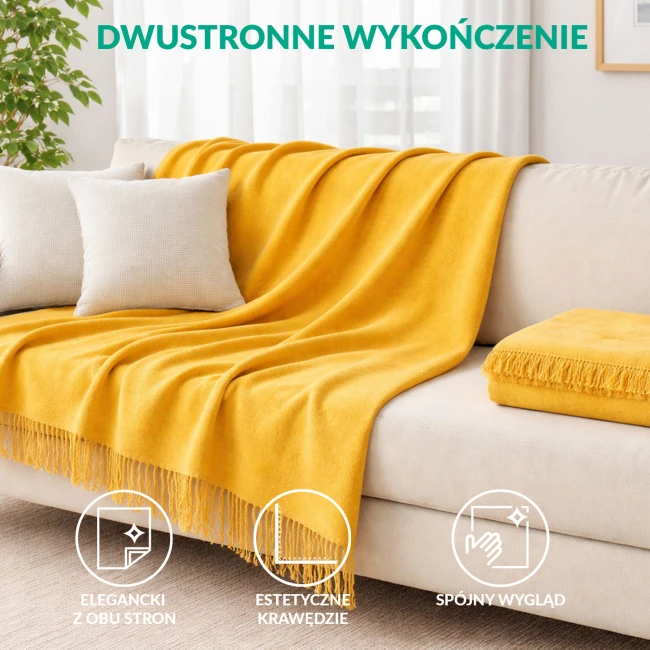 Koc bawełniany 150x200 cm w kolorze żółtym z frędzlami, leżący na beżowej sofie. Wyraźna struktura materiału, frędzle na dolnej krawędzi. W tle widoczna roślina doniczkowa oraz obrazki na ścianie, co tworzy przytulną atmosferę wnętrza.