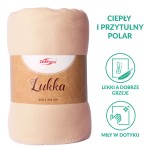 Koc polarowy Lukka w kolorze beżowym, o wymiarach 150x200 cm, zwinięty, widoczny z przodu. Materiał miękki, o gładkiej fakturze. Widoczna etykieta z nazwą produktu oraz wymiarami. Tło jednostajne, co podkreśla detail produktu.