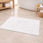Dywanik łazienkowy 50x70 cm w kolorze białym, o gramaturze 500 g/m², z wyraźnym wzorem stóp. Ułożony na płytkach, z prostokątnym kształtem i teksturowaną powierzchnią. Tło jasne, z naturalnym oświetleniem.