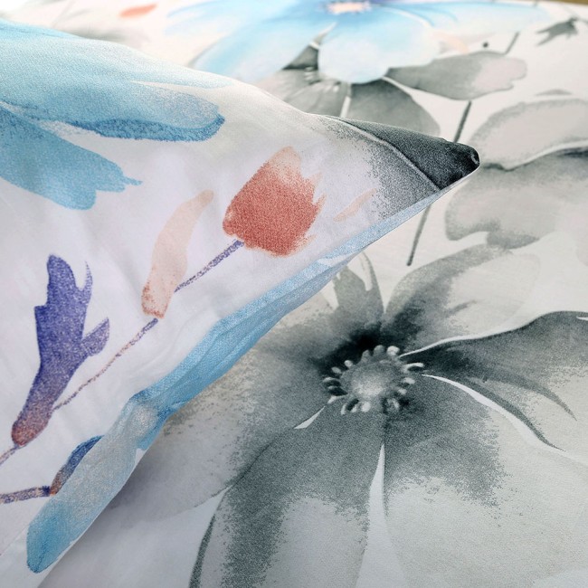 Pościel satyna bawełniana 160x200 w białym kolorze z dużymi pastelowymi niebieskimi i różowymi kwiatami. Zbliżenie na poszewkę poduszki i fragment kołdry, z widocznymi detalami wzoru i subtelnymi odcieniami.