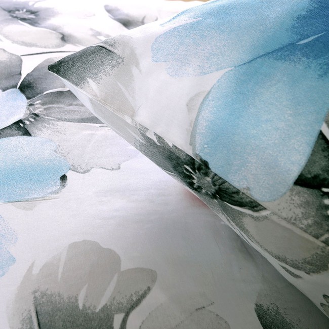 Pościel satyna bawełniana 160x200 w białym kolorze, zdobiona dużymi pastelowymi niebieskimi kwiatami. Kąt ujęcia zbliżony na poduszkę i poszewkę, ukazujący subtelne detale wzoru na gładkiej tkaninie.