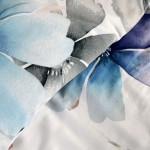 Pościel satynowa w kolorze białym, z dużymi pastelowymi niebieskimi kwiatami. Materiał gładki, z delikatnym połyskiem. Widok na fragment poszwy na kołdrę i poduszki, ukazujący szczegóły wzoru oraz kolorystykę.