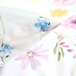 Pościel satyna bawełniana 160x200 Vellia w białym kolorze z pastelowymi, akwarelowymi kwiatami. Widoczna poduszka z różowymi i błękitnymi kwiatami na jasnym tle. Ujęcie z bliska, ukazujące detale wzoru i fakturę materiału.