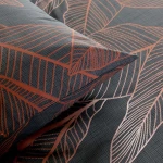 Pościel bawełniana 180x200 cm w ciemno szarym kolorze z miedzianym wzorem liści. Widoczne poduszki i poszwy z geometrycznym wzorem, ułożone na złożonej pościeli, z matową fakturą materiału.