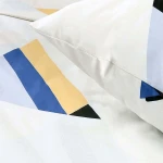 Pościel bawełniana 160x200 w białym kolorze z geometrycznym wzorem w odcieniach niebieskiego, żółtego i czarnego. Widok z góry, poduszka i kołdra leżą na płasko, ukazując detale wzoru oraz teksturę materiału.