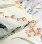 Pościel bawełniana 140x200 Herbalia w kremowym kolorze z botanicznym wzorem kwiatowym. Widoczne detale poduszki z nadrukiem w odcieniach pomarańczowego i zieleni, na tle delikatnych liści i kwiatów. Produkt leżący na gładkiej powierzchni.