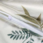 Pościel bawełniana 140x200 cm w kolorze kremowym z botanicznym wzorem kwiatowym. Widoczny zamek błyskawiczny, delikatna tekstura materiału, subtelne zielone i brązowe liście, idealna do sypialni.