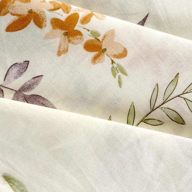 Pościel bawełniana 140x200 w kremowym kolorze z botanicznym wzorem kwiatowym. Widoczne delikatne kwiaty w odcieniach pomarańczowym i fioletowym oraz liście. Tkanina gładka, o naturalnej fakturze, ułożona w złożone fałdy.