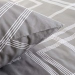 Pościel bawełniana 140x200 w szarym kolorze z minimalistycznym białym geometrycznym wzorem. Poduszka z ostrym zakończeniem, leży na poszewce, która ukazuje wzór na całej powierzchni. Tło jest jednolite, co podkreśla detale.